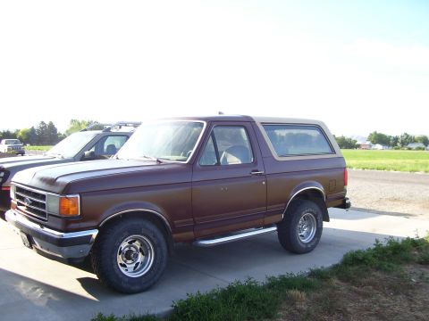 1990 Ford Bronco - Brown 1990 Ford Bronco parked on a paved surface with another vehicle beside it.