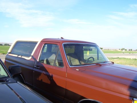 1990 Ford Bronco - A two-tone Ford Bronco is parked outdoors under a bright blue sky with some clouds.