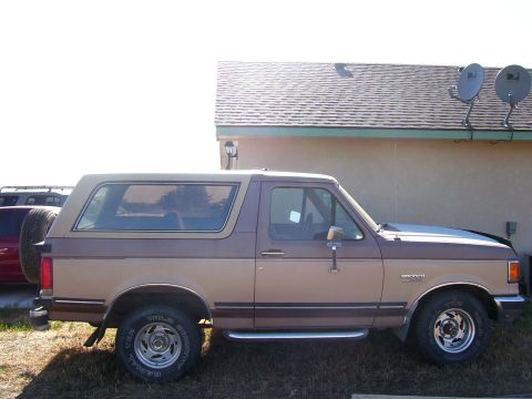 1990 Ford Bronco - A two-tone brown Ford Bronco is parked outside a building with satellite dishes on the roof.