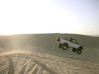 1996 Ford Bronco - A 1996 Ford Bronco soars through the air during a jump over a sand dune.