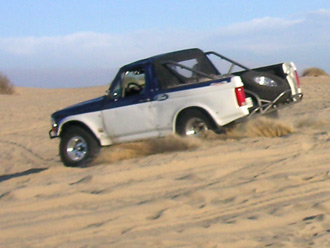 1996 Ford Bronco - This 1996 Ford Bronco is shown navigating sandy terrain, equipped with a roll cage and spare tire.