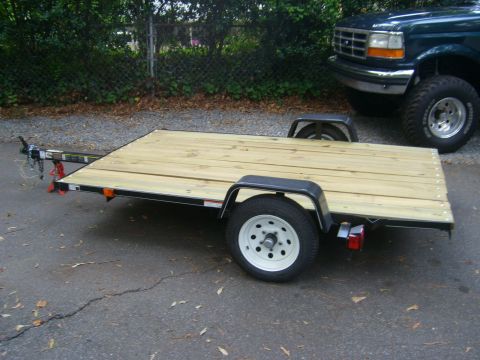 1994 Ford Bronco - A utility trailer sits on asphalt next to the front of a dark blue Ford F-Series truck.