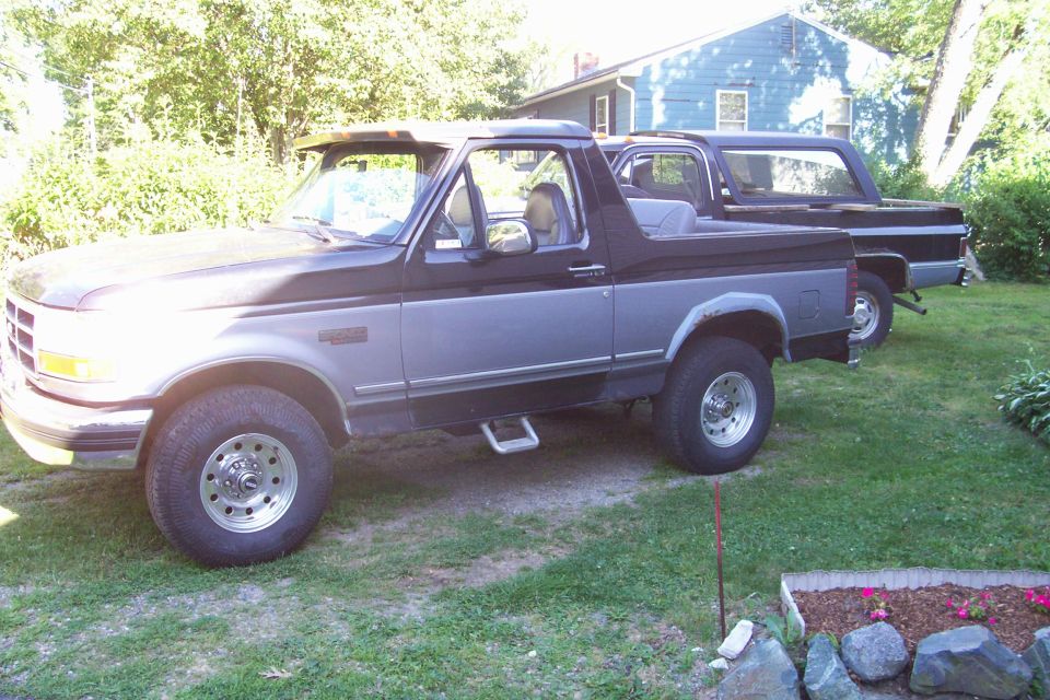 Two-tone Ford Bronco parked in a yard with a house in the background