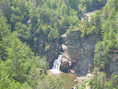 1985 Ford LTD Crown Victoria - A scenic view of a waterfall flowing into a pool, framed by dense forest and rocky outcrops.