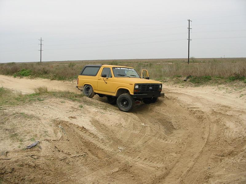 Yellow two-door Ford Bronco SUV parked on a dirt trail in flat open country
