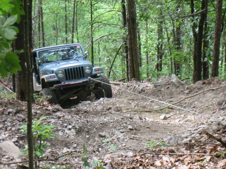 Blue Jeep Wrangler on a wooded trail, being pulled by a rope