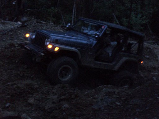 Dark blue Jeep Wrangler on a dirt trail at night, front lights on