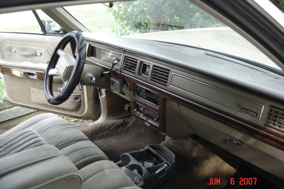 Tan interior of Ford LTD Crown Victoria showing dash with woodgrain trim, steering wheel, and cloth bench seat