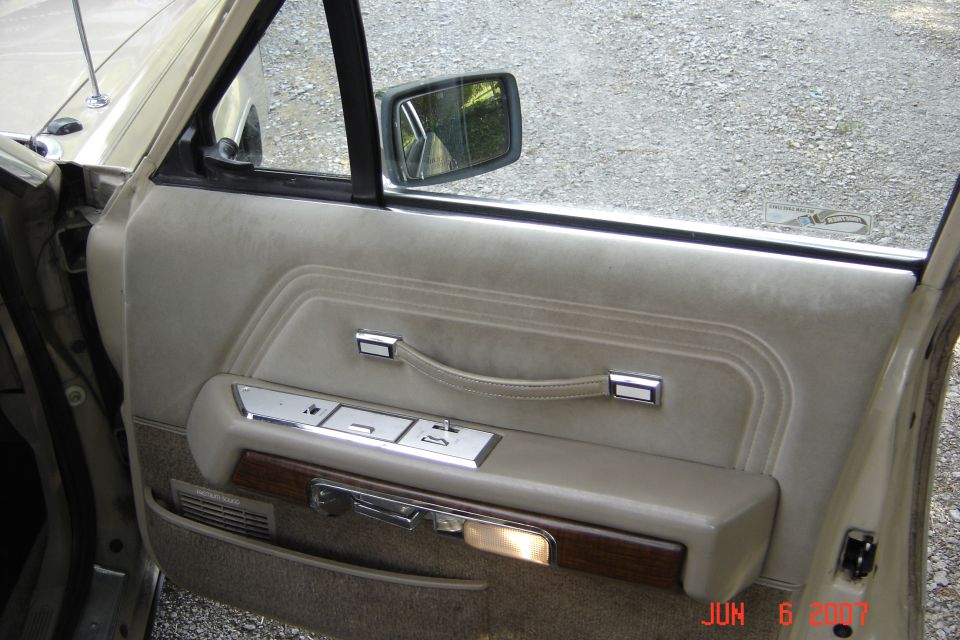 Open driver's door showing tan interior panel with chrome switches, woodgrain trim and courtesy light
