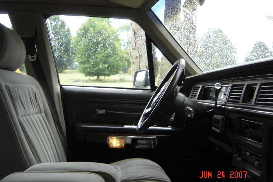 Gray cloth interior and black steering wheel of a Crown Victoria seen through the open driver's door