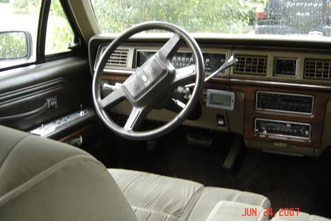 1989 Ford Crown Victoria LTD - The interior of a car shows a tan dashboard with wood trim and a large steering wheel, with a digital display mounted below the vents.