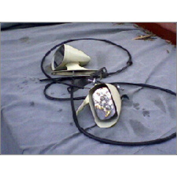 Two beige side mirrors with black wiring on a gray tarp