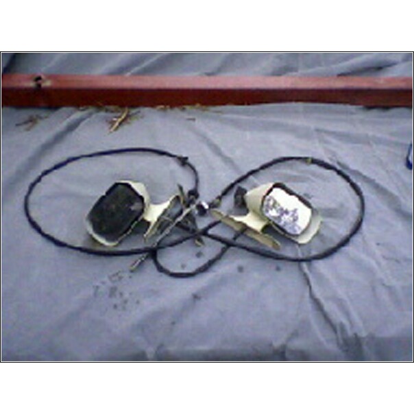 Two side mirrors with beige housings and black backing, connected by wires, lying on a grey cloth
