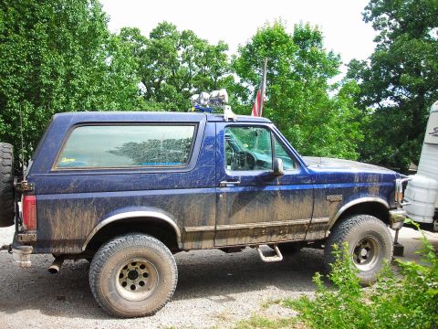 1994 Ford Bronco - Side view of a muddy blue 1994 Ford Bronco with a spare tire mounted on the rear.