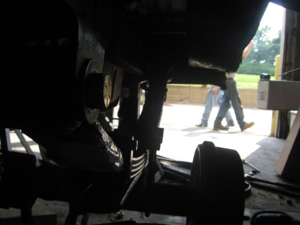 Underneath a vehicle showing leaf springs and drum in silhouette, with people walking outside a shop door