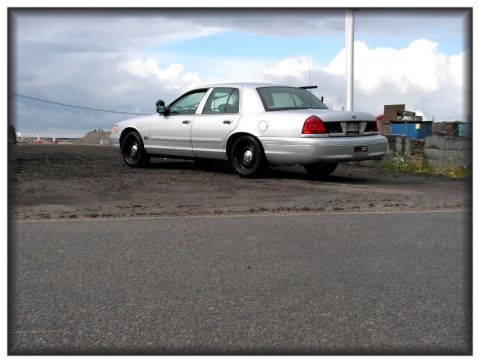 1998 Ford Crown Victoria - A silver 1998 Ford Crown Victoria sedan is parked on a dirt lot with a cloudy sky overhead.