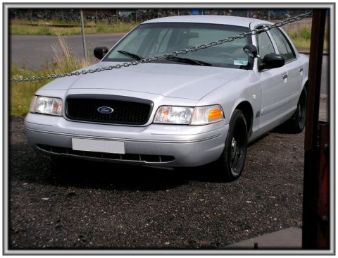1998 Ford Crown Victoria - This Ford Crown Victoria has a black grille and black wheels, with a chain draped across its front.