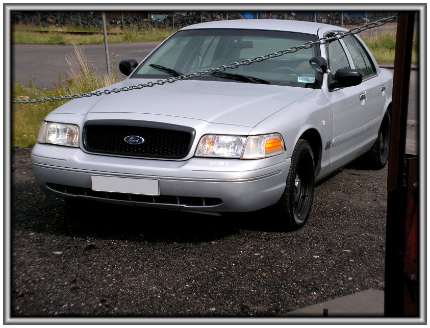 Silver Ford Crown Victoria with black grille and black wheels. Chain across the front