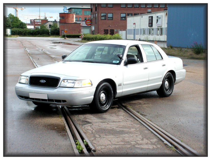 White sedan with black wheels on train tracks, front 3/4 view