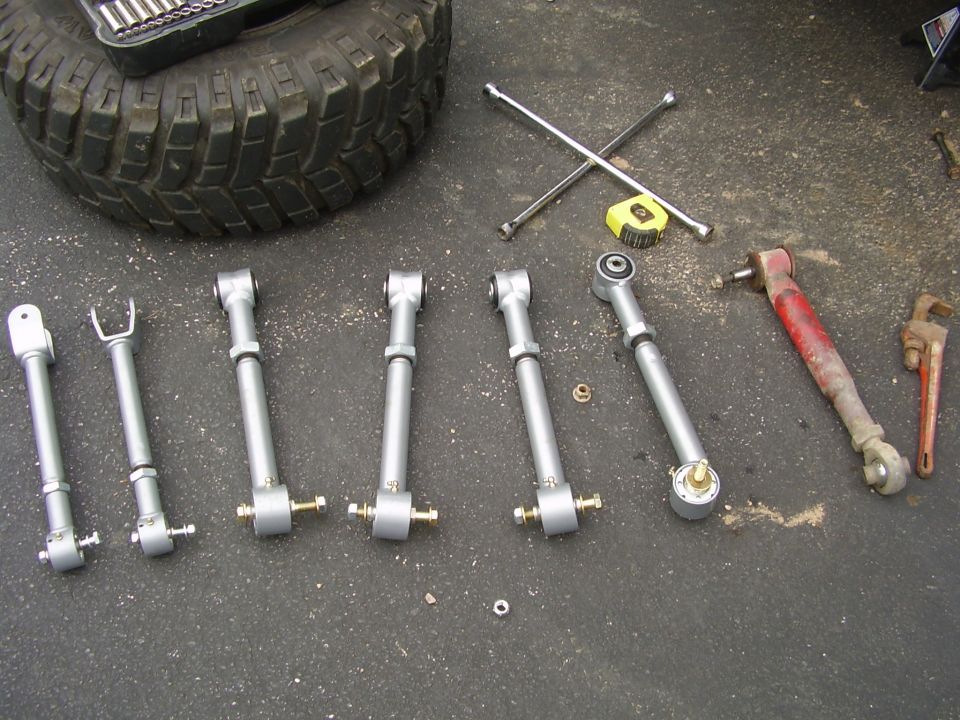 Suspension control arms, tire, and tools laid out on pavement