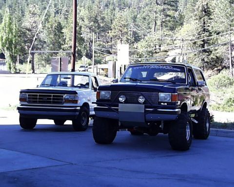1989 Ford Bronco - Two Ford Broncos are parked in an outdoor lot with trees in the background.