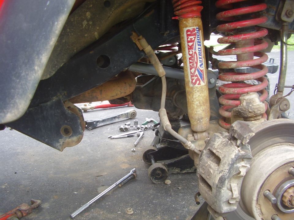 Jeep suspension with Skyjacker Nitro 8000 shock and red coil spring, brake caliper, and tools on ground