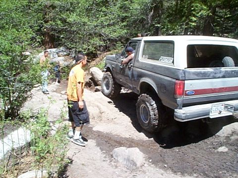 1989 Ford Bronco - A 1989 Ford Bronco navigates a rocky off-road trail with a driver and passengers.