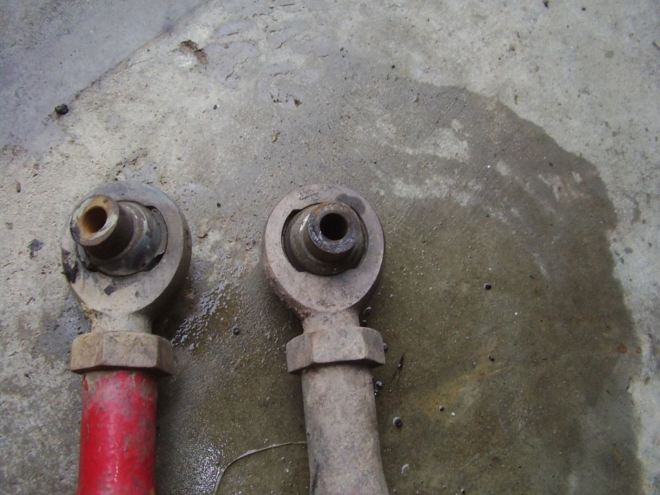two suspension control arms, one red and one gray, resting on a wet concrete surface