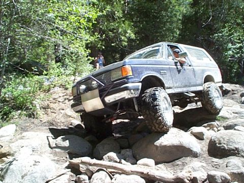 1989 Ford Bronco - This lifted blue Ford Bronco is shown tackling a challenging rocky terrain on an off-road trail.