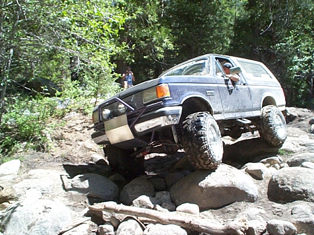 Blue Ford Bronco navigating a rocky off-road trail, lifted with large tires