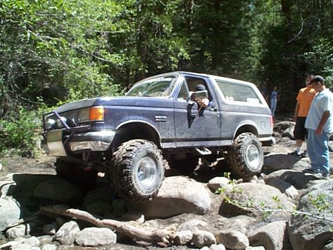 1989 Ford Bronco - This 1989 Ford Bronco is shown off-roading over large rocks in a wooded area.