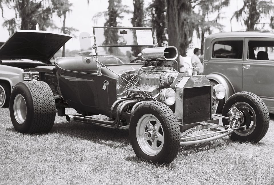 hot rod roadster with supercharger, parked on grass next to a sedan and a pickup truck