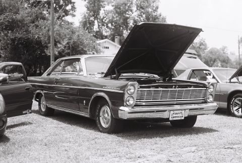 1973 Ford Ranchero - A dark-colored 1965 Ford Galaxie 500 is parked with its hood up, alongside other vehicles.