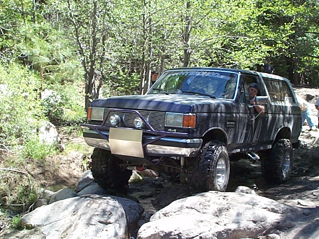 Dark blue Ford Bronco with off-road tires navigating rocky terrain. Driver visible