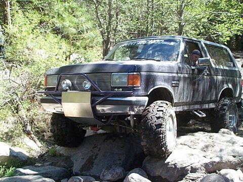 1989 Ford Bronco - This modified Ford Bronco is navigating a rocky trail, showing its off-road capabilities.