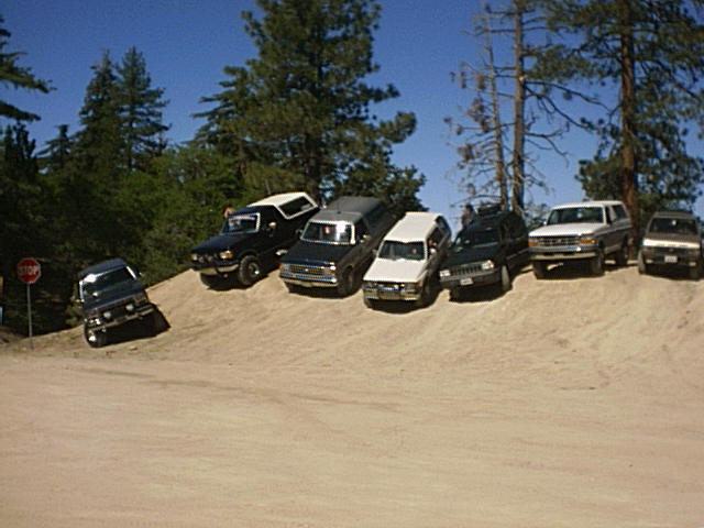 Several SUVs parked on a dirt incline with trees and a blue sky in the background