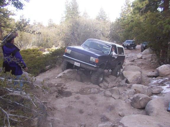 Dark blue Ford Bronco navigating a rocky trail, with another SUV visible in the background
