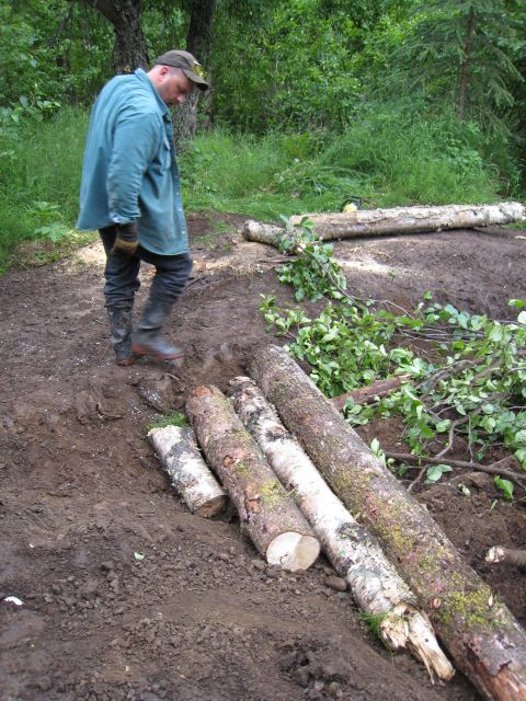 2000 Ford E350 - A man stands near several large logs that have been placed on a dirt path in a wooded area.