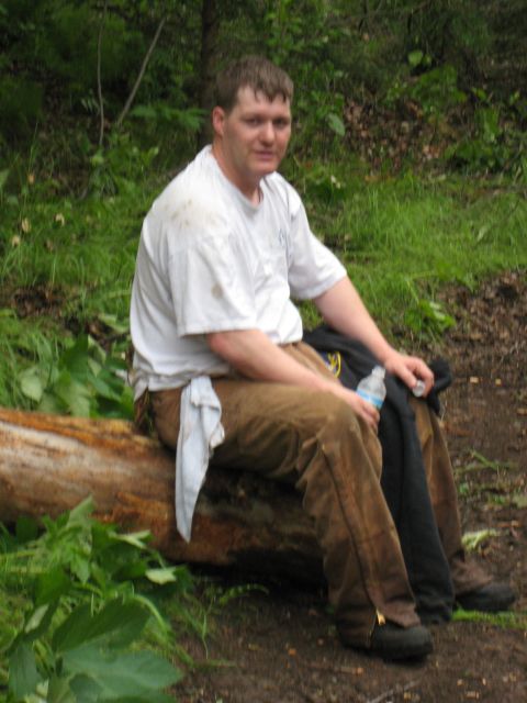 2000 Ford E350 - Man takes a break sitting on a log in a wooded outdoor setting.