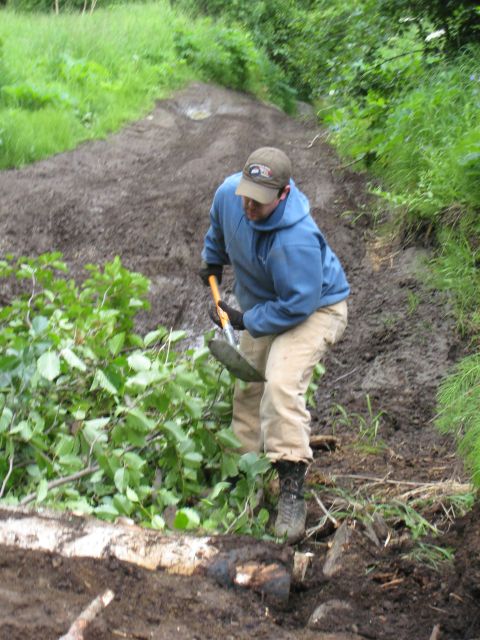 2000 Ford E350 - A person is digging in the dirt with a shovel, surrounded by vegetation and logs.