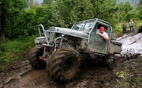 2000 Ford E350 - This heavily modified off-road vehicle navigates a challenging muddy terrain with spectators nearby.