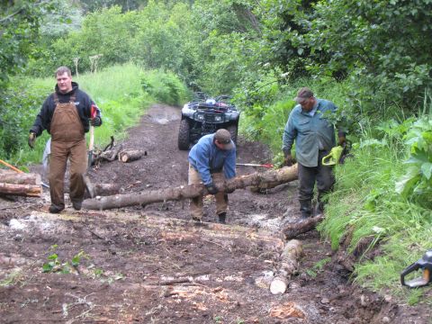 2000 Ford E350 - Men work to clear a muddy path, moving logs with an ATV nearby.