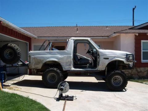 1995 Ford Bronco - This modified white SUV, possibly undergoing custom work, is shown from the side with its doors open and a rollcage installed.