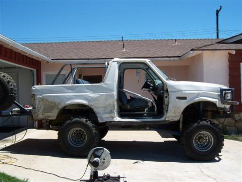 1995 Ford Bronco - Side view of a modified 1995 Ford Bronco undergoing work, a rollcage and external spare tire.