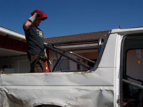 1995 Ford Bronco - A man installs a custom rollcage into a white Ford Bronco with visible body damage.
