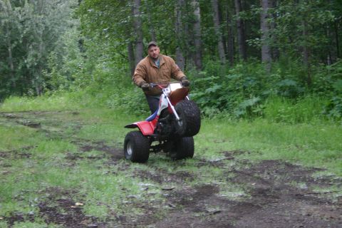 2003 Jeep TJ - A man rides a red and white three-wheeled ATV on a muddy path surrounded by trees.