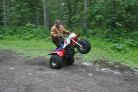 2003 Jeep TJ - Rider on a red three-wheeled ATV lifts the front wheels off the ground while riding on a dirt path.
