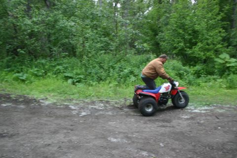 2003 Jeep TJ - A person rides a three-wheeled all-terrain vehicle through a wooded area on a dirt path.