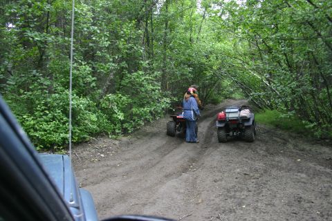 2003 Jeep TJ - Two ATVs are stopped on a dirt road in a wooded area, with two people standing near one of them.
