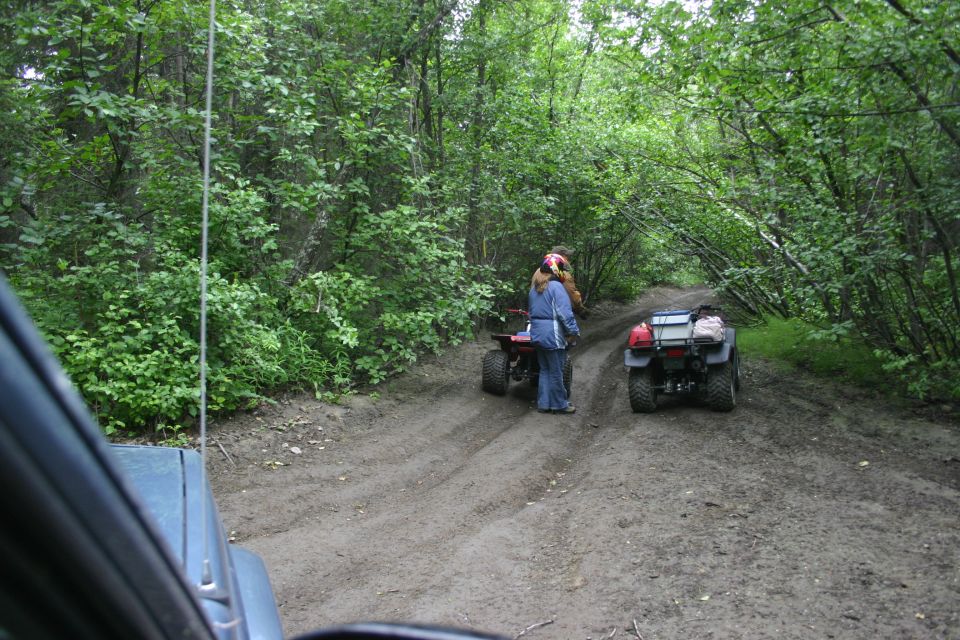 Two ATVs on a muddy dirt road surrounded by trees. One ATV is red, the other is black